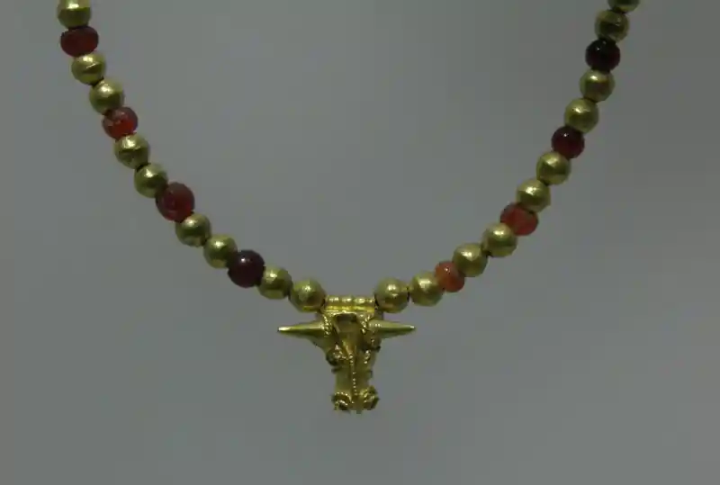 A gold necklace with red and gold beads and bullhead pendant A gold necklace with red and gold beads and bullhead pendant